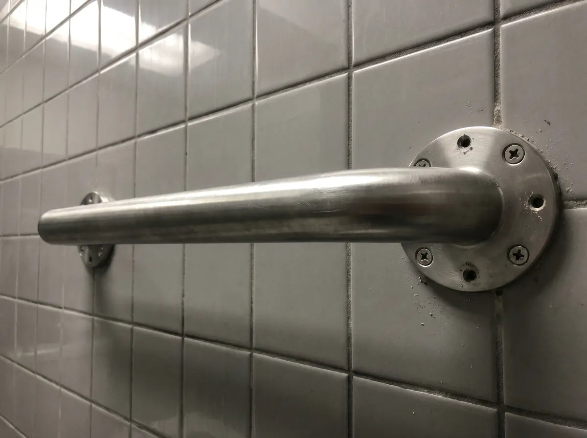 A clinical stainless-steel grab bar bolted into bathroom tile with visible drill holes